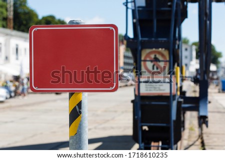 an empty red sign in front of crane constructions on a quayside