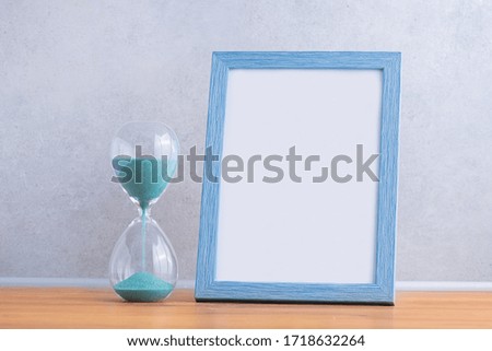 Blue wooden frame for photo with hourglass on a wall background. Concept of the transience of time. 