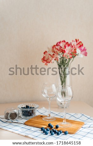 Two glasses on a cutting board, lying next to fresh blueberries on a background of a vase with a bouquet of flowers.