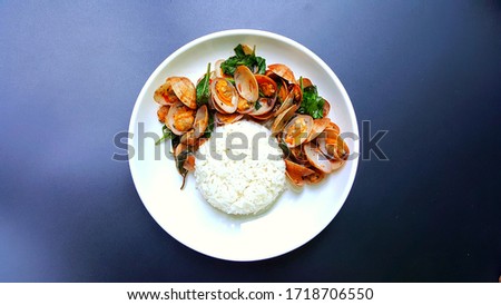 Stir-fried clams with spices and basil on a white plate Is a popular Thai food eaten with steamed rice. Spicy taste