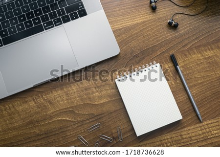 Laptop computer with an open notebook,pen and headphones on a wooden surface