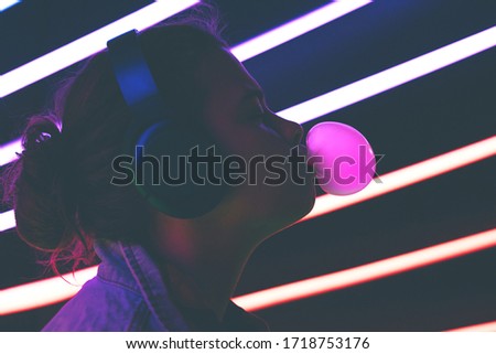 Young girl profile blowing bubble gum and looking at the frame illuminated neon dark light. Millennial woman.
