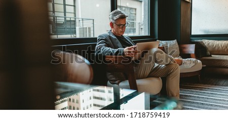 Mature businessman sitting in office lobby with a laptop. Male executive working in office lounge. Royalty-Free Stock Photo #1718759419