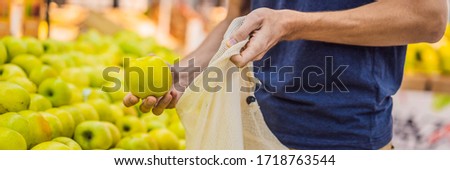 Man chooses apples in a supermarket without using a plastic bag. Reusable bag for buying vegetables. Zero waste concept BANNER, LONG FORMAT