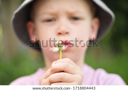 boy with hat blows the dandelion empty