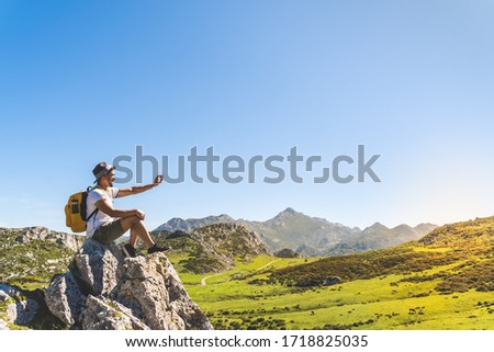 Latin Man Taking Picture to the Sunset in the Mountain Wearing Backpack. Young Man Sitting in a Rock Looking the Sunset in the Mountain . Young Man Hiking Alone. Lifestyle Concept.