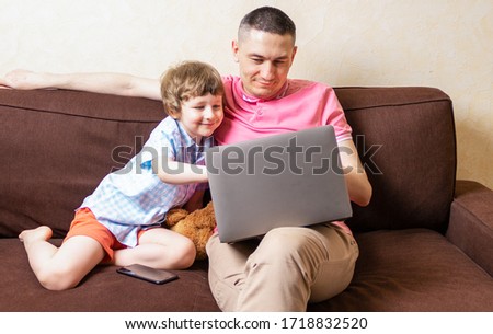 Happy young father sit on computer using laptop relax with preschooler son have fun together, smiling dad and little boy child enjoy weekend at home rest on sofa busy with gadgets. Online education.