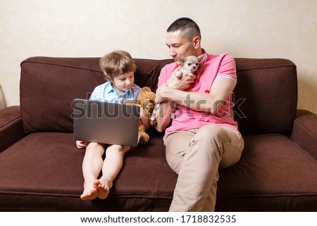 Happy young father sit on couch using laptop relax with preschooler son holding puppy chihuahua have fun together, smiling dad and little boy child enjoy weekend home rest on sofa busy with gadgets