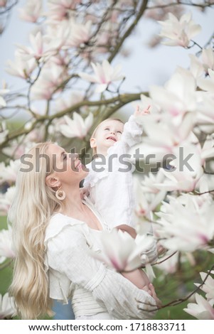 Mother and daughter in magnolia flowers  wearing white dresses on a sunny spring day