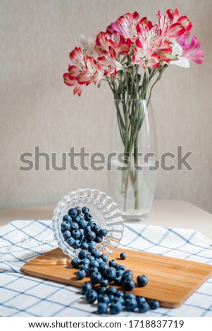 Blueberries dropped from a glass onto a kitchen board. Against the background of a vase with a bouquet of flowers. Diet. Healthy eating