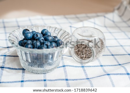 Fresh blueberry in a glass cup, and next to it in a jar are chia seeds. Concept of healthy and dieting eating.