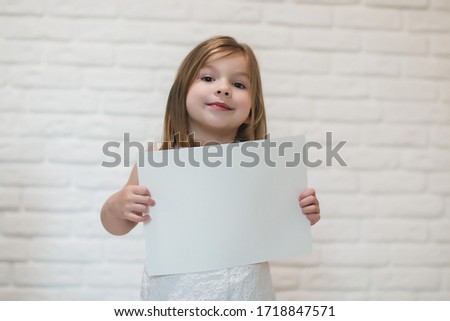 little girl near the white brick wall holding a white empty paper sheet