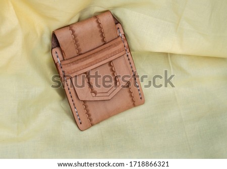 A hand tooled leather cell phone case displayed on yellow fabric. Bokeh. Royalty-Free Stock Photo #1718866321