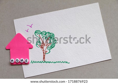 Pink paper house next to childrens drawing of wood and birds. Stay at Home picture. Coronavirus concept.