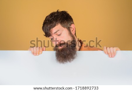 Advertising board. Copy space. Bearded man looking on blank board. Space for text. Man holds empty board. Advertising banner. Man shows empty board. Ready for your text.