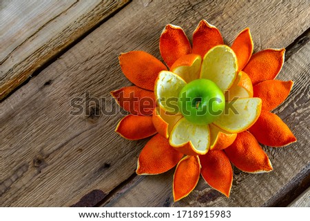 The apple with orange peels like a flower are located on the table from rough boards