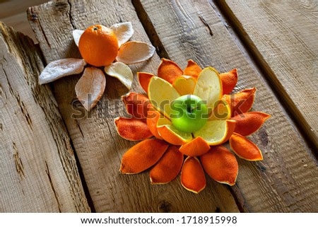 The apple and the orange with orange peels like a flower are located on the table from rough boards