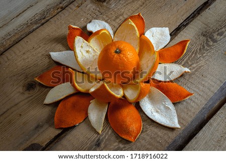 The orange with orange peels like a flower are located on the table from rough boards
