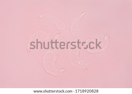 Squeezed cosmetic clear cream gel texture. Close up photo of transparent drop of skin care product. High Quality transparent gel with bubbles closeup on pink background.