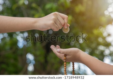 Islamic zakat or sadaka, adult giving money to child.Close-up of a hand giving coin on bokeh green background.