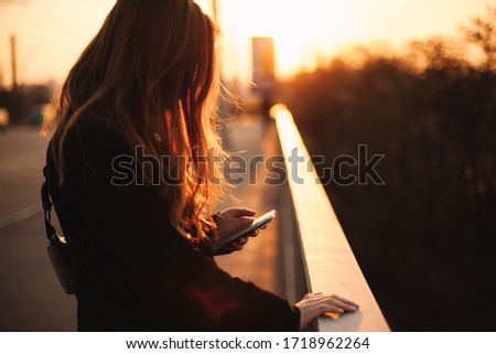 Young woman using smart phone while holding railing standing on bridge in city at sunset Royalty-Free Stock Photo #1718962264