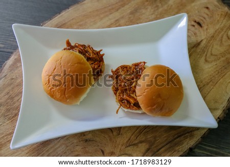 Two buns with pulled chicken with sweet barbeque sauce on a white platter. Pulled chicken sandwiches.