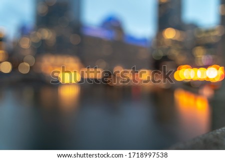 An out of focus skyline background photo of buildings along the Chicago River in downtown at night with the street lights creating round bokeh balls and reflections in the water.