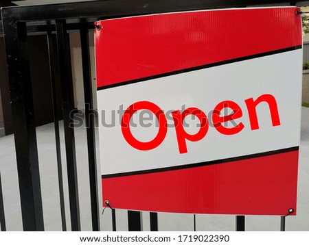 Open text on announcement red and white board hanging on metal fence of a restaurant or a shop.