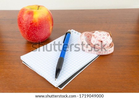 An apple, a notebook, a measuring tape, a pencil lie on a table.