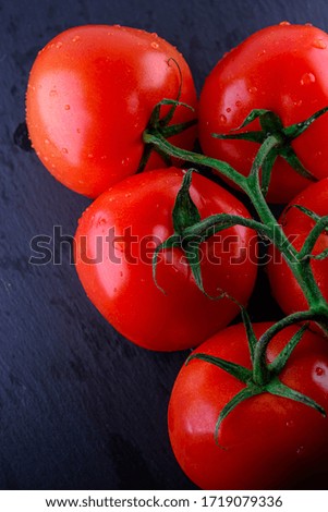 Group of fresh ripe whole tomatoes with water drops on vintage black surface. Food advertisement design. Food background.