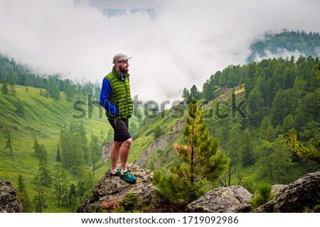 A man stands on a hill in front of a foggy mountain valley. Foggy weather high in the mountains in summer