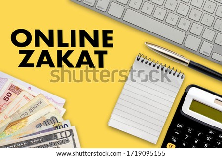 ONLINE ZAKAT (islamic tax)  text with notepad, calculator, keyboard, multi banknote or currency and fountain pen on yellow background. Zakat (Islamic Tax), Business and Islamic concept