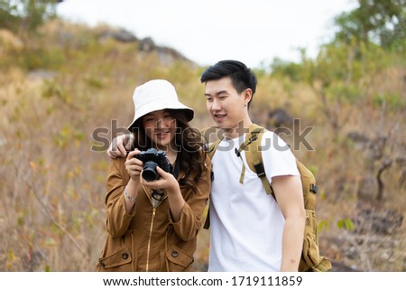 Beautiful Asian couple in love on vacation. Hikers with backpacks relaxing and enjoying view