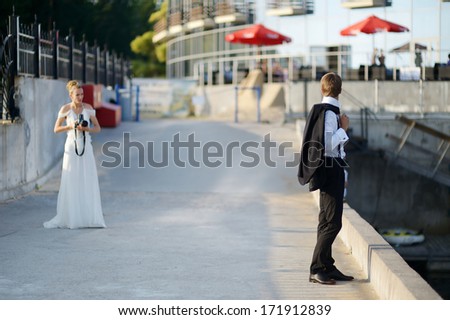Groom posing while his bride is shooting with an old camera