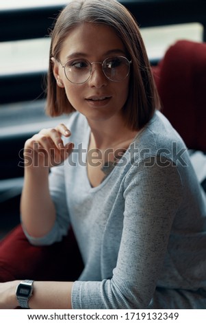 Portrait of an attractive girl sitting in a red cozy chair opposite a large window. Loft Interior