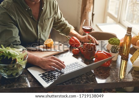 Cropped photo of a male cook sitting in front of his laptop in the kitchen