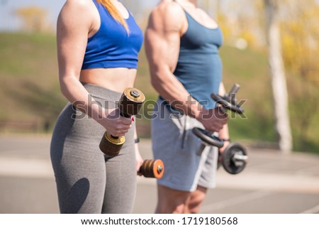 Athletic guy and girl doing exercises with dumbbells at the sports field. Health care.