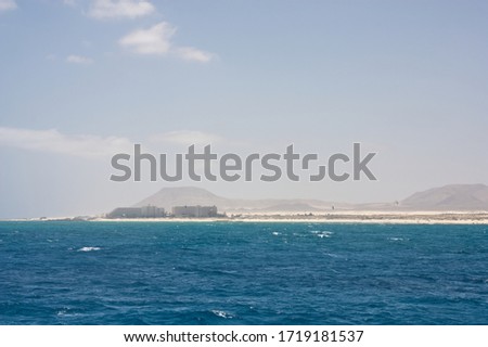 Seascape with white capped waves and fluffy clouds looking toward the Las Dunas area of Corralejo Fuertaventura from the sea. Space left for copy text.