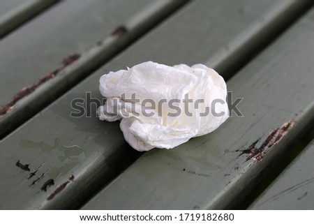 A wrapped tissue paper ball on a grey / green painted wooden bench in Zürich, Switzerland. Closeup image. Concept of flu, sickness, allergy, mess, etc. Closeup color image photographed spring 2020.