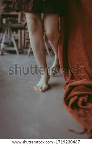 A close-up of female feet walking on a concrete floor in a ceramic studio. Skin tanned legs of a beautiful woman wearing a short a burgundy linen dress with orange plaid. Lifestyle concept in pottery