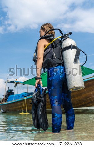 Stock photo of a concentrated girl in the water with a wetsuit, diving goggles, flippers and diving tank. She is next to some longtail boats in Thailand.