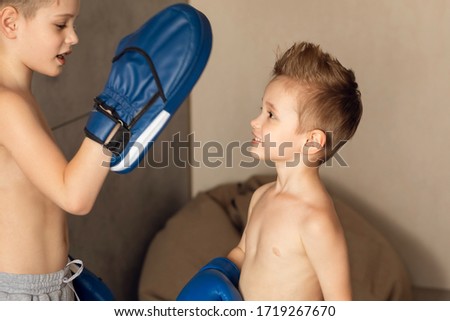 Big brother teaches little brother boxing technique. Self-isolation during quarantine. A smaller child listens with interest. Children have blue boxing accessories