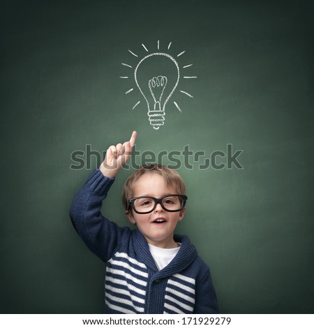 Schoolboy standing in front of a blackboard with a bright idea light bulb above his head concept for innovation, imagination and inspirational ideas Royalty-Free Stock Photo #171929279