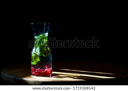 Black background and glass, drink with mint and pomegranate beans, stands opposite suns rays. Useful water.