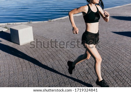 Photo of an athletic girl dressed in black during a morning jog on a city beach in the morning.