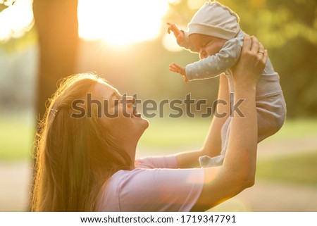 Young mother holds up two-month-old newborn baby in the summer green park. Moments of happy motherhood
