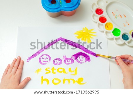 Top view child is drawing family under a roof with words Stay Home on sheet of paper.