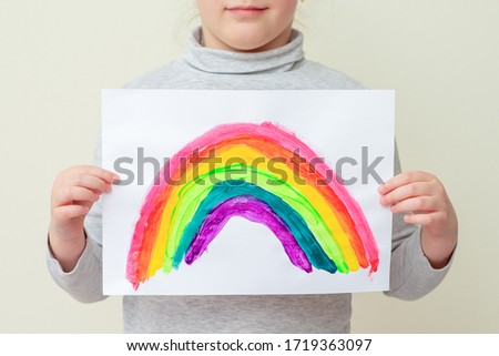 Little girl holds drawn rainbow on sheet of paper, close-up.