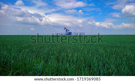 Oil pumpjack in the wheat field. Crude oil and food production synergy. 