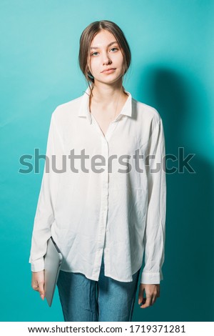 young girl in a white shirt and jeans with a laptop on a blue background in the studio